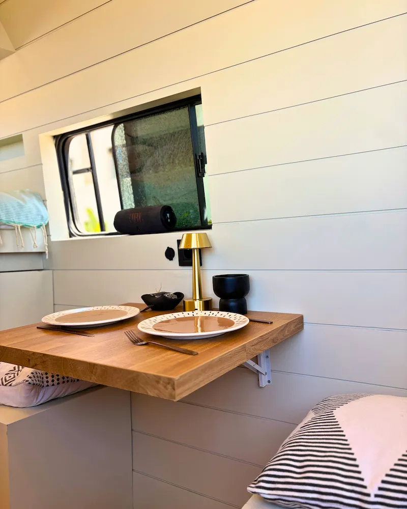 Table pliante en bois avec vaisselle dans van aménagé, coin repas cosy pour deux personnes au Maroc.