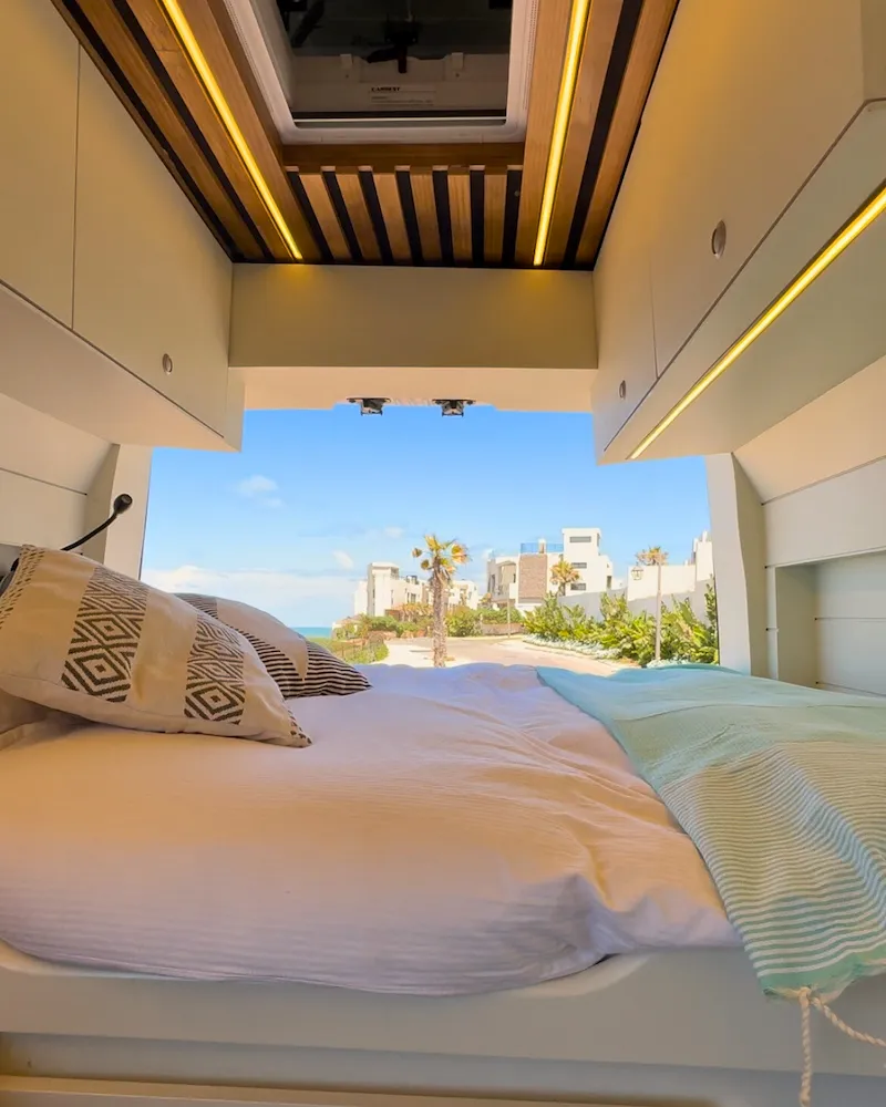 Lit du van ouvert sur une vue mer et palmiers, ambiance vacances et liberté au Maroc.